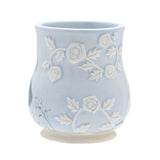 Alice in Wonderland embossed earthenware mug in pale blue with raised white rose and leaf details and a faint sketched Alice motif, shown on a plain white background.