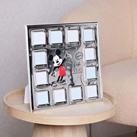 Silver-plated square photo frame with twelve month-labelled windows around a central Mickey Mouse design, displayed on a side table beside an armchair.