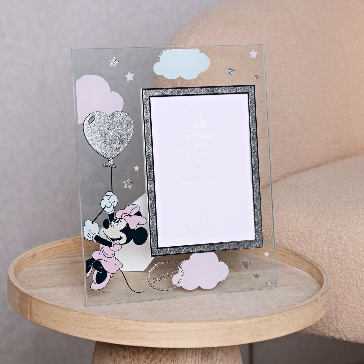 Clear glass 7 x 5in photo frame with Minnie Mouse on a silver glitter heart balloon, pink and mint clouds, stars, silver glitter border, and "Baby Girl" wreath, shown on a wooden table.