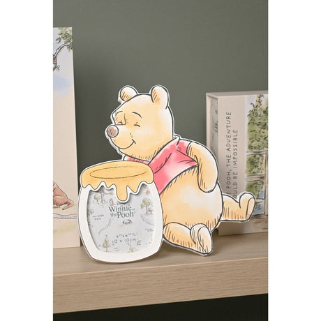 Winnie the Pooh shaped wooden photo frame in orange and white, with Pooh leaning beside a honey pot frame, displayed on a shelf with books.