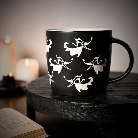 Nightmare Before Christmas Zero Stoneware Mug with matt black ceramic body, white Zero ghost dog silhouettes, white interior, and black handle, shown on a dark table beside candles and an open book.