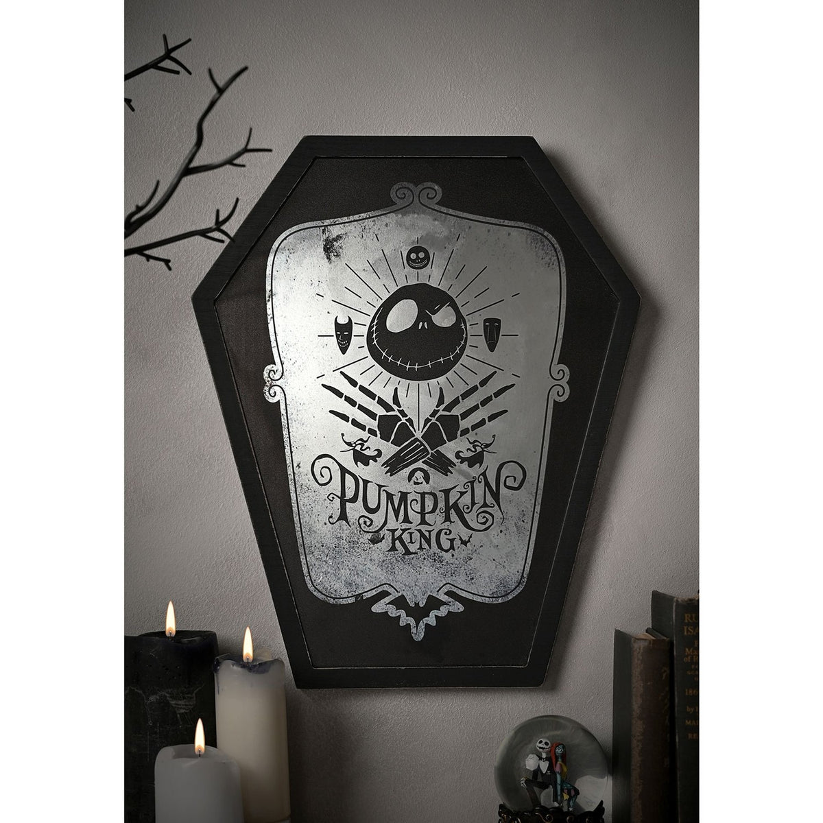 Coffin-shaped black wooden wall plaque with mirrored centre featuring Jack Skellington's skull, crossed skeletal hands, and "Pumpkin King" text, shown mounted on a wall above candles and books.