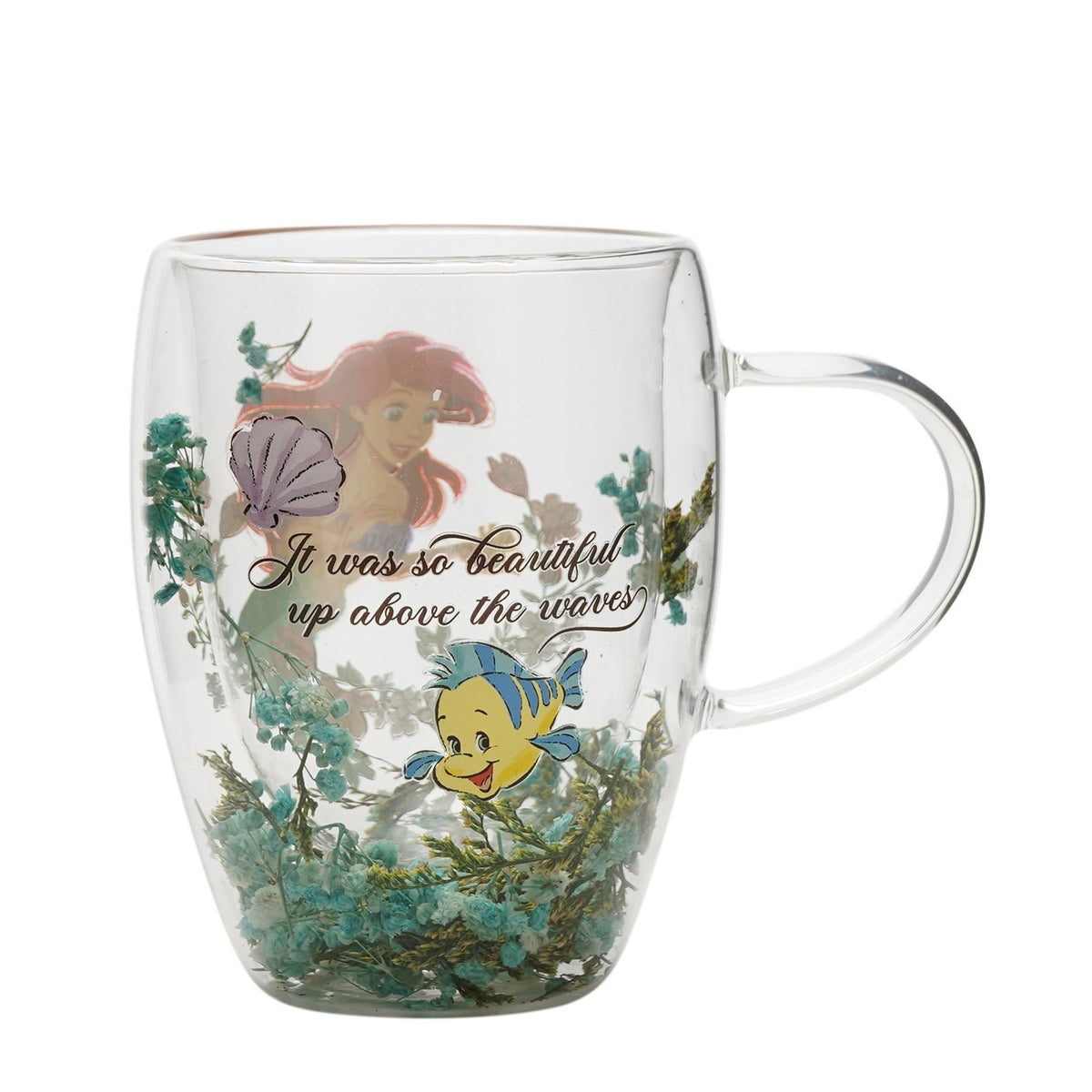 Clear double-wall glass mug with handle, featuring Ariel and a purple shell, "It was so beautiful up above the waves" script, Flounder, and green dried flowers at the base, on a white background.