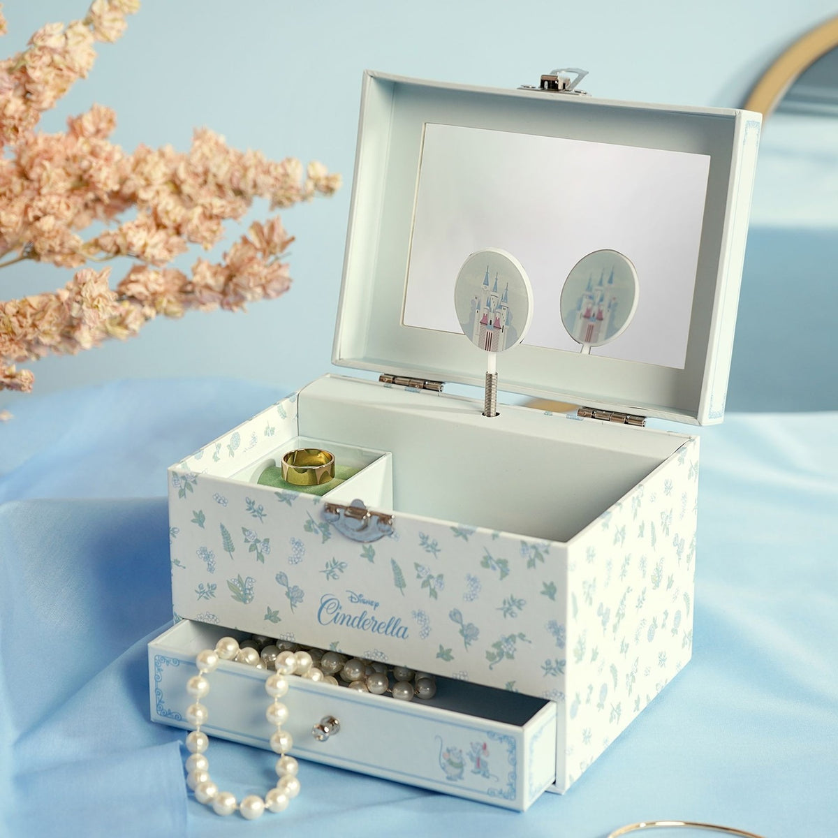Pastel Princess Cinderella musical jewellery box, open lid with mirror and spinning castle figure, floral-print exterior, pull-out drawer with pearl necklace, on a light blue backdrop.