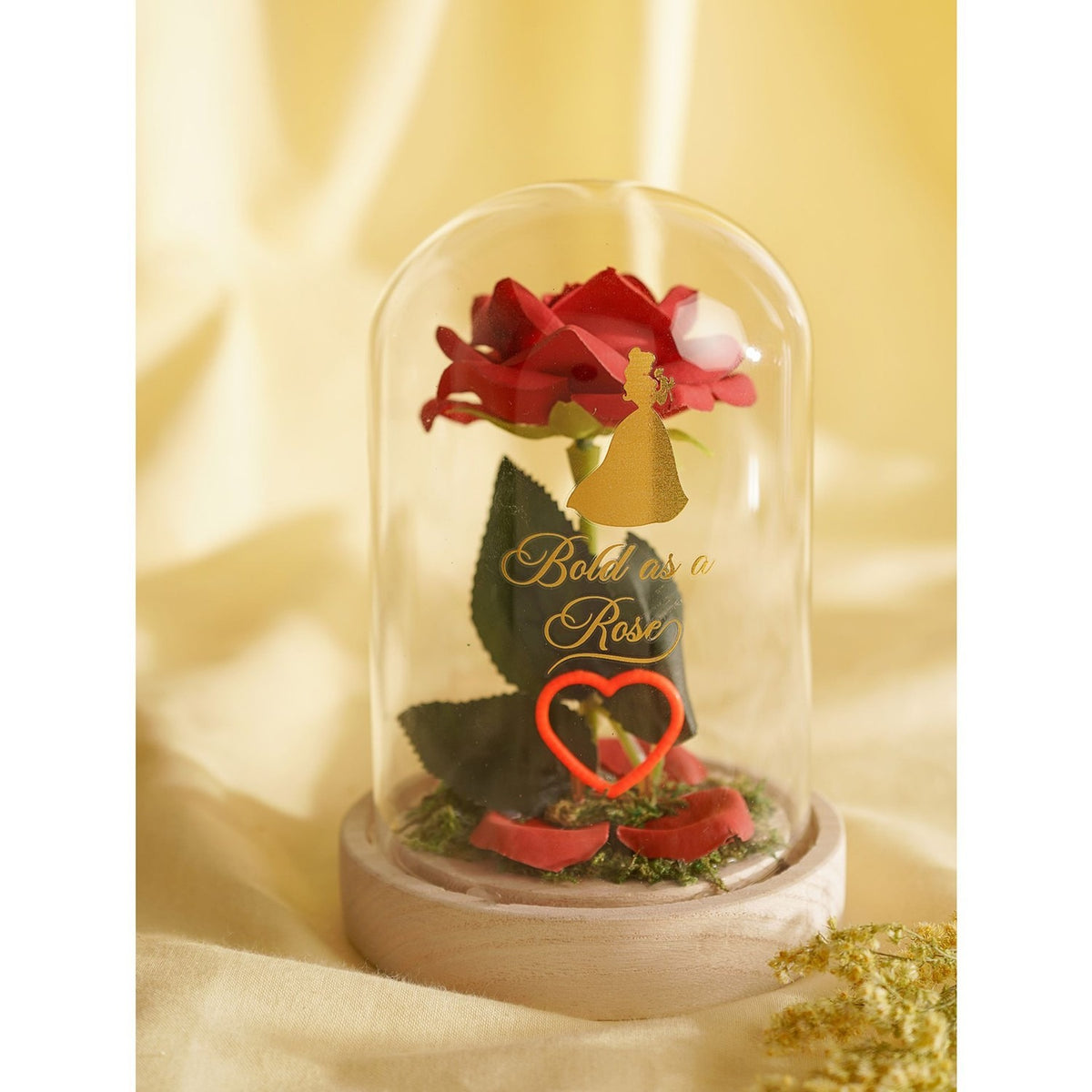 Belle-themed light-up cloche with a red rose under a clear dome, gold Belle silhouette, Bold as a Rose script, glowing red heart outline, and green leaves on a round wooden base.