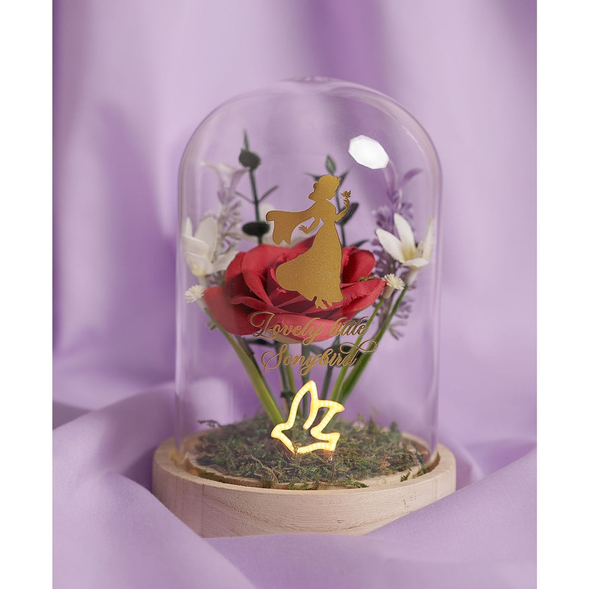 Snow White Pastel Florals Cloche: gold Snow White silhouette with songbird over a red rose, pastel blooms, and moss base under a clear arched dome on a wooden stand.