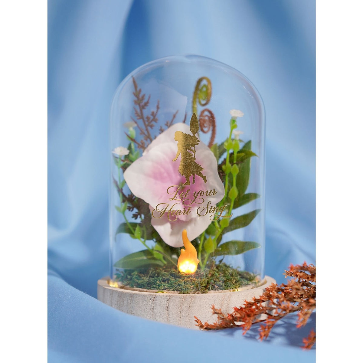 Light-up glass cloche on wooden base with pink and white bloom, foliage, gold spiral accents, glowing LED flame, and gold princess silhouette decal.