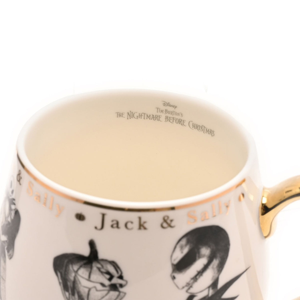 Close-up of cream porcelain Jack & Sally mug with gold handle, showing gold "Jack & Sally" lettering and black sketched character artwork below the rim.