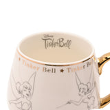 Close-up of white porcelain Tinker Bell mug with gold handle and rim, pencil-style sketches of Tinker Bell, gold star name band, and "Disney TinkerBell" script printed inside the rim.
