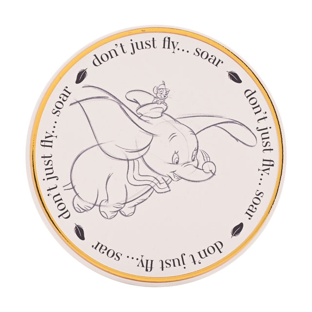 Round white stoneware coaster with a pencil-style sketch of Dumbo flying and a mouse on his head, a gold rim, and "don't just fly... soar" text with feather icons around the edge.