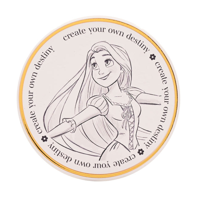 Round white stoneware coaster with a pencil-sketch drawing of Rapunzel, arms outspread, bordered by a gold ring and repeated text "create your own destiny" on a plain background.