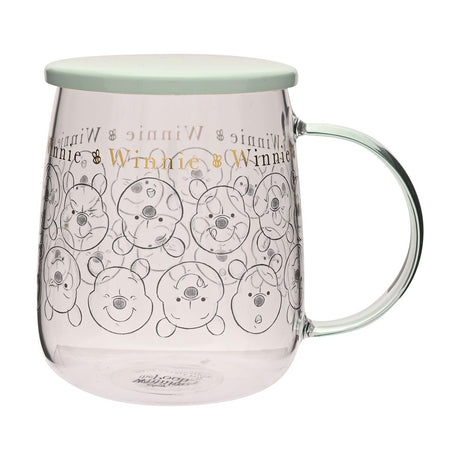Clear glass mug with green lid and handle, featuring repeated Winnie the Pooh face line drawings and gold "Winnie" lettering with bee motifs, 570ml, shown on a plain white background.