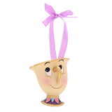 Resin cream teacup Christmas ornament with gold rim, rosy cheeks, purple, pink and blue banded base, hanging on a lilac ribbon against a white background.
