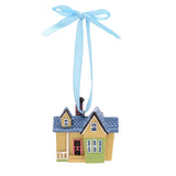 Resin house hanging Christmas decoration with blue shingled roof, cream and green walls, pink door, brick chimney and pale blue ribbon bow, on a white background.