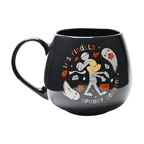 Black round stoneware mug featuring Mickey Mouse as a mummy with a pumpkin bucket, ghosts and autumn leaves, with "it's finally spooky season" text, on a white background.