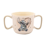 Cream porcelain baby mug with two sage-green handles, featuring Stitch hugging a green rag doll and "dream big little one" script, shown on a plain white background.