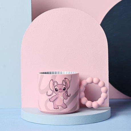 Pink ceramic Stitch Angel mug with a chunky round bobble handle, featuring grey swirl patterns and a striped white interior, displayed on a light pastel backdrop.
