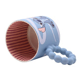 Ceramic mug lying on its side showing Stitch waving on a pastel blue body with white swirls, a chunky blue bobble handle, and red and cream striped interior, on a white background.