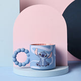 Blue ceramic Stitch mug with white swirl pattern, chunky bobble handle, and red-striped interior, displayed on a stand against a pink and blue backdrop.