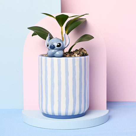 Cylindrical stoneware planter with blue and white vertical stripes and a solid blue base, featuring a 3D glossy grey-blue Stitch figure perched on the rim beside a faux green plant.