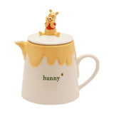 Winnie the Pooh Honey Pot stoneware teapot with cream body, yellow drip glaze, "hunny" text and bee detail, topped with a seated Pooh figure lid, shown on a white background.
