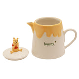 Cream and yellow stoneware teapot shaped like a Winnie the Pooh honey pot, featuring a dripping honey glaze, "hunny" text, bee detail, and a sculpted Pooh figure on the removable lid.