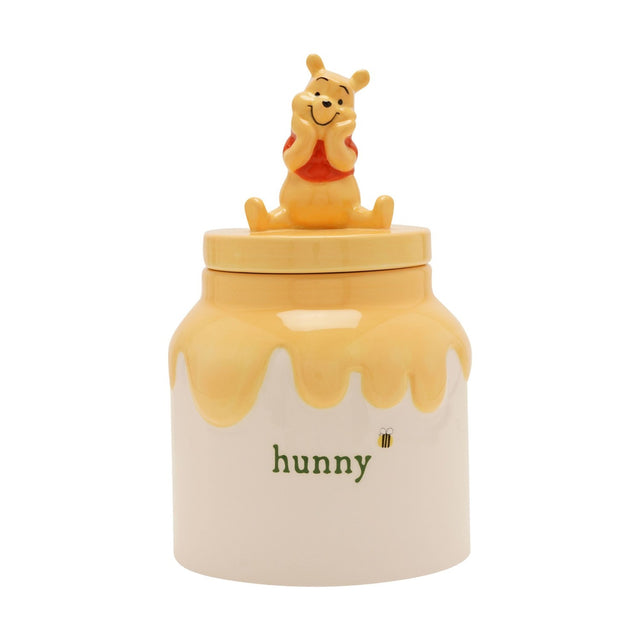 Winnie the Pooh ceramic honey pot storage jar in cream and yellow, with Pooh seated on the lid, "hunny" lettering and a bee motif, on a plain white background.