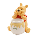 Winnie the Pooh Honey Pot resin storage box in pale yellow and white, bear resting chin on paws over an open pot marked "hunny", shown on a plain white background.