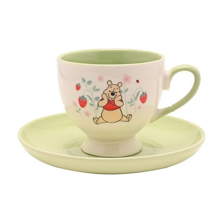 Winnie the Pooh porcelain cup and saucer, 240ml, cream cup with green rim, handle and interior, footed base, decorated with Pooh, strawberries and blossoms, on a plain white background.