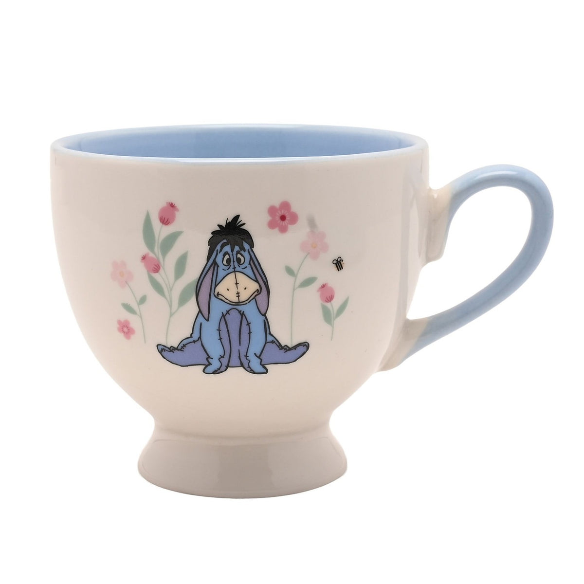 Footed porcelain cup in cream with pale blue handle and interior, featuring Eeyore among pink flowers and a bee, set on a plain white background.