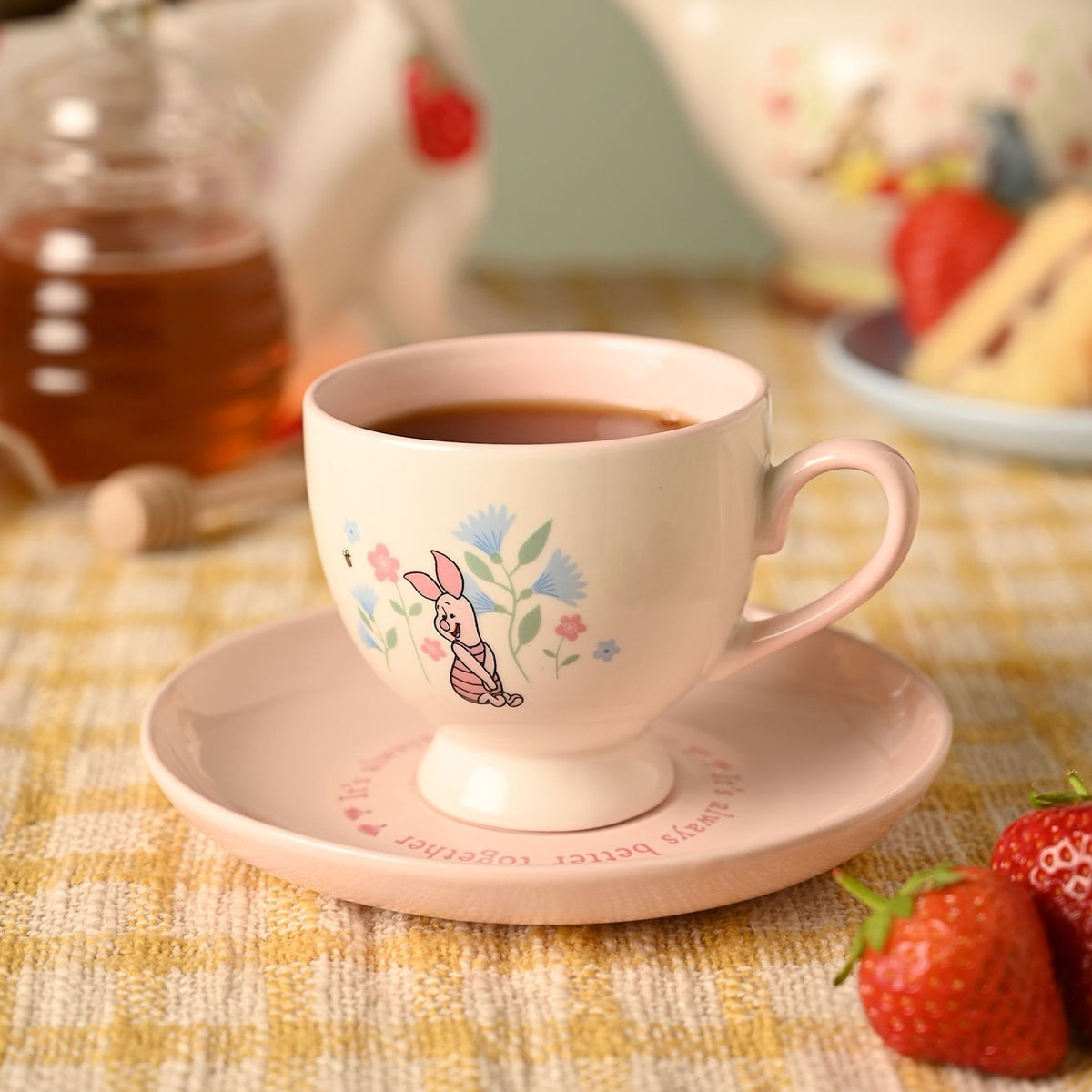 Winnie the Pooh Piglet porcelain cup and saucer in cream and pink, footed teacup with pink handle filled with tea, floral Piglet design, shown on pink saucer with script text amid a tea table setting.