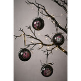 Set of four glossy black round tree baubles hanging from decorative branches with fairy lights, each printed with a pink, white and pale blue Nightmare Before Christmas character panel.