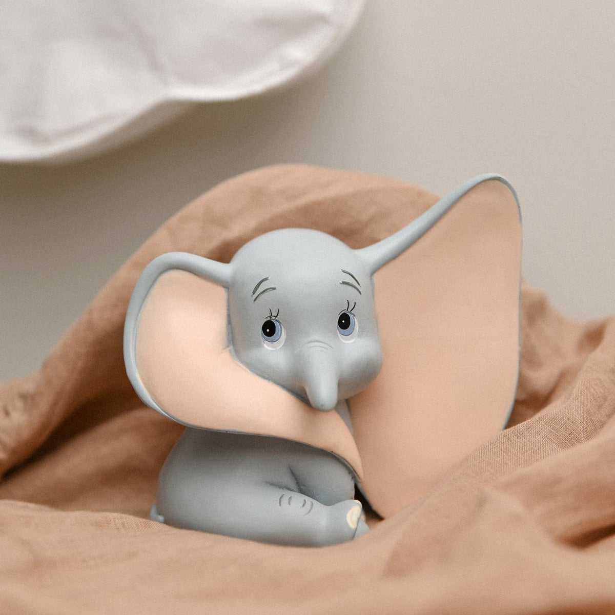 Sitting Dumbo Elephant resin money box in matt grey with pale pink ear interiors, shown nestled in soft fabric against a neutral background.
