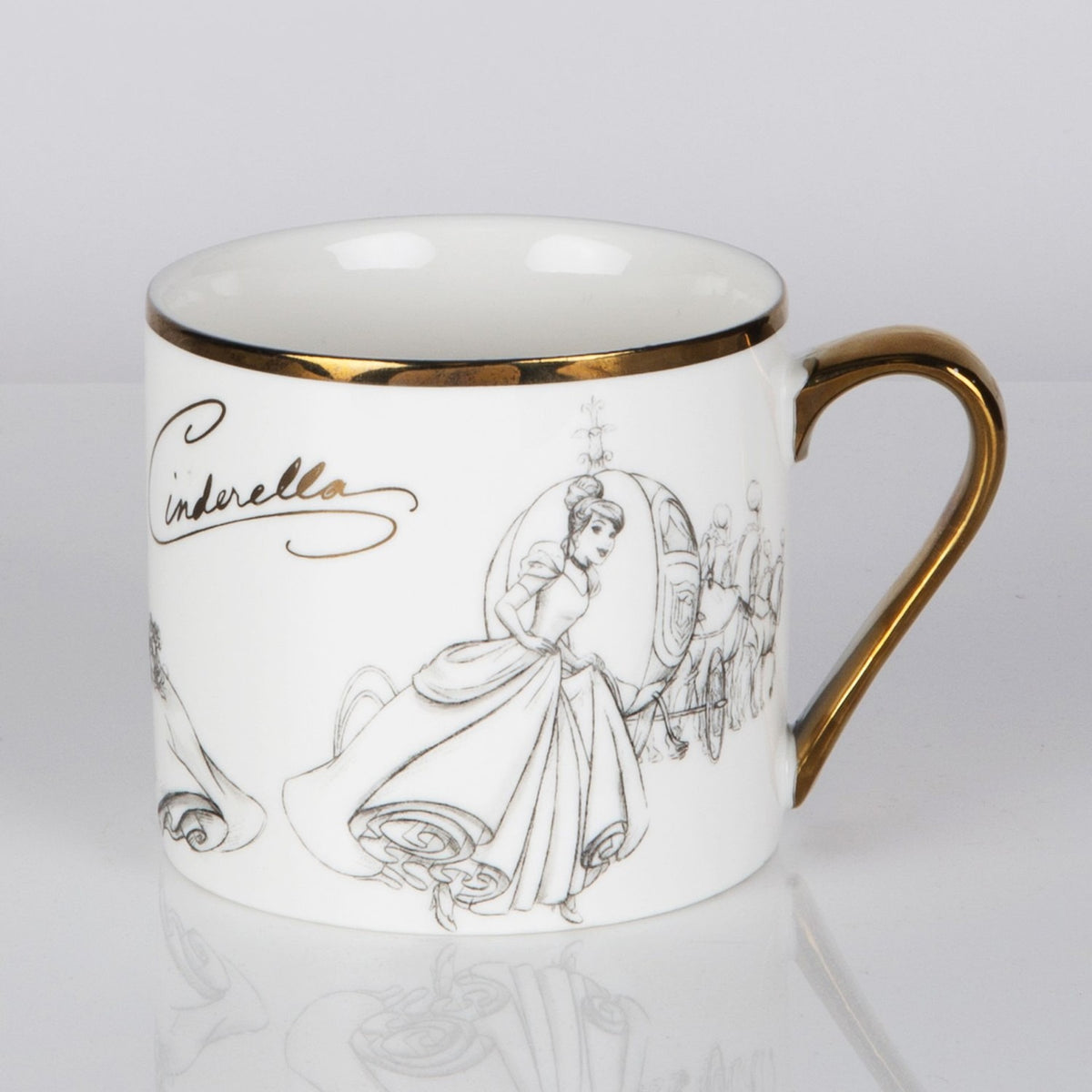 White porcelain mug with gold rim and handle, featuring grey pencil-style sketches of Cinderella in her gown and coach, with her name in gold script, on a plain background.