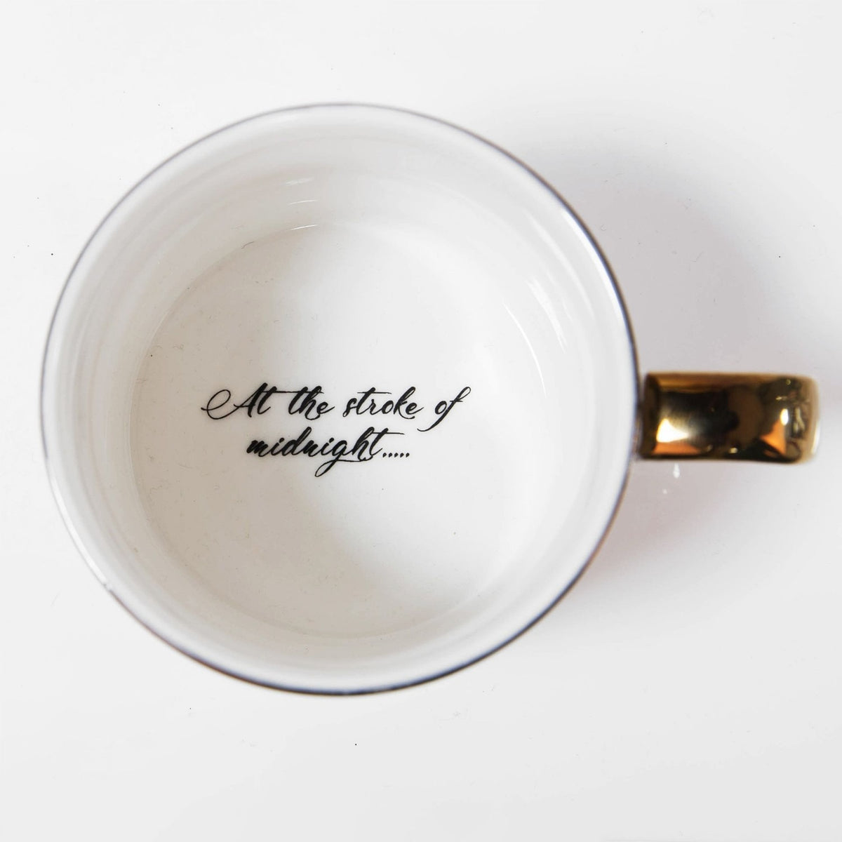 Top-down view of the white Cinderella Sketch Classic porcelain mug, showing the glossy interior printed with At the stroke of midnight..... in black script, with gold rim and handle.