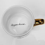 Belle Sketched Classic Collectable Porcelain Mug in white, overhead view showing the glossy interior with "live your dreams…." script and a gold handle, on a plain white background.