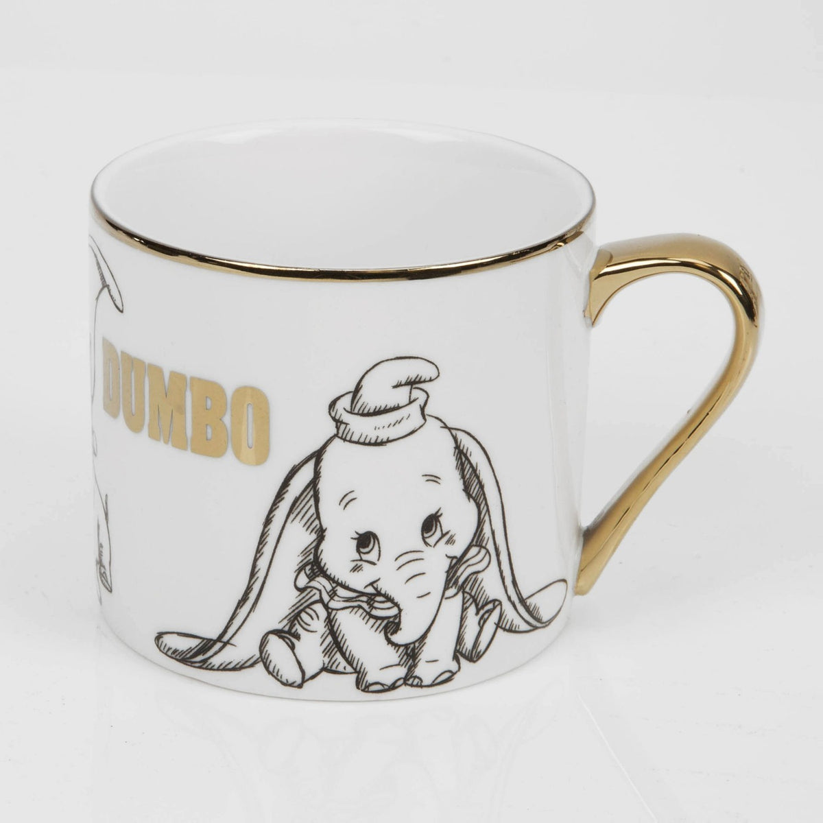 White porcelain Dumbo mug with gold rim and handle, featuring black sketched artwork of Dumbo and "DUMBO" lettered in gold, shown on a plain white background.