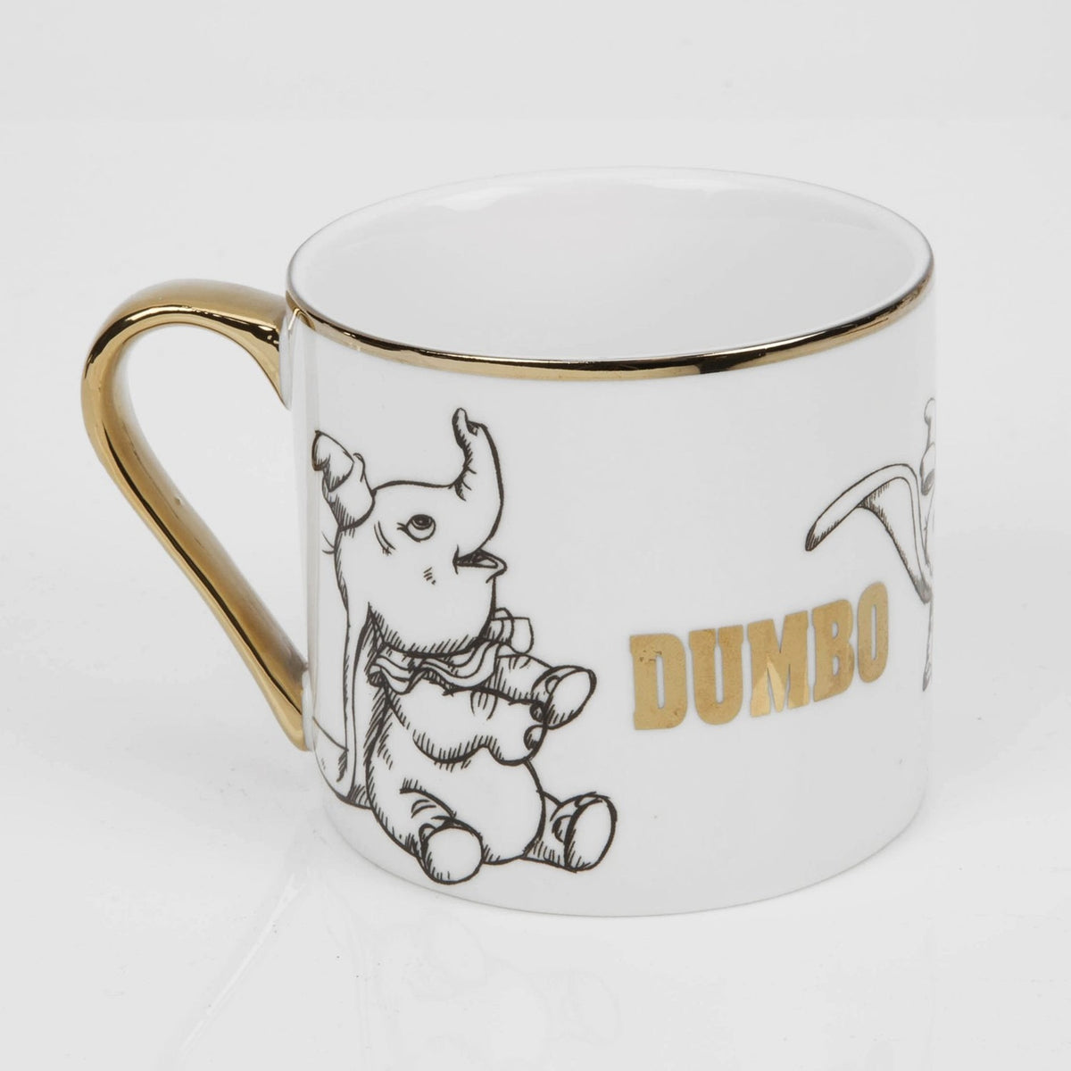 White porcelain Dumbo mug with gold handle and rim, featuring black sketched elephant illustrations and "DUMBO" in gold lettering, shown on a plain white background.