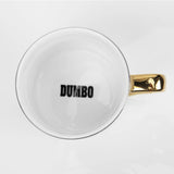 Top-down view of the Dumbo porcelain mug showing the white interior with "DUMBO" printed in black and the gold handle, on a plain background.