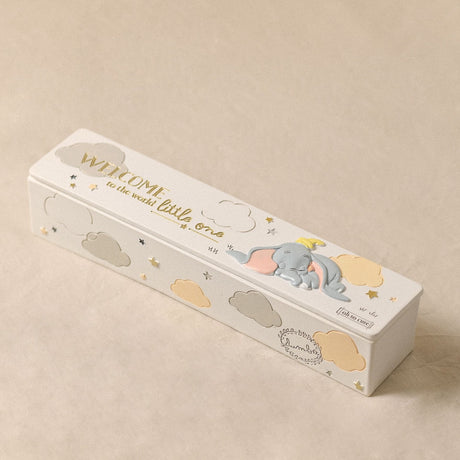 White rectangular keepsake box with sleeping Dumbo in relief, grey and yellow clouds, gold "Welcome to the world little one" text, set on a plain beige background.