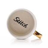 Top-down view of the Stitch Classic porcelain mug showing a white gloss interior base with "Stitch" in black script and a gold handle, on a plain white background.