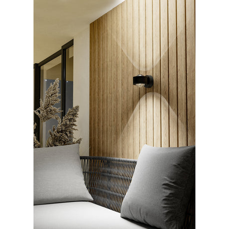 Dilvelle LED Outdoor Wall Light in anthracite aluminium, mounted on a wood-slat wall above a grey cushioned outdoor sofa, casting up-and-down light beams.
