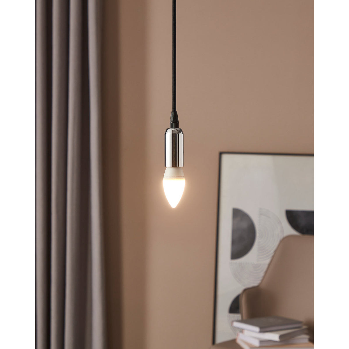 Dimmable LED candle bulb with E14 cap and opal shade, glowing warm white in a pendant light fitting against a pink wall, with framed art nearby.