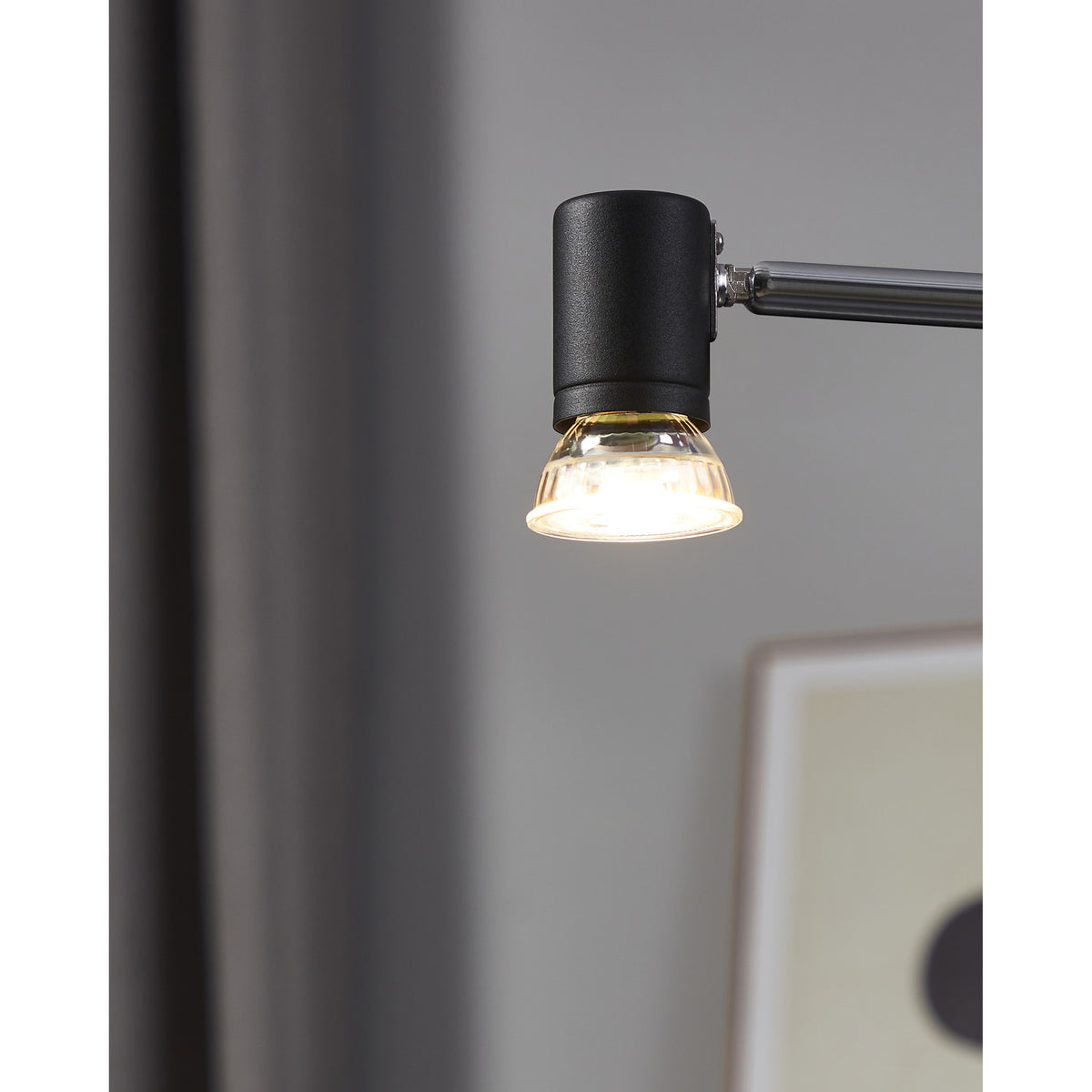 Dimmable GU10 LED bulb with clear faceted glass reflector, fitted into a matte black adjustable wall light, glowing warm white in a living room setting.