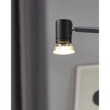 Dimmable GU10 LED bulb with clear faceted glass reflector, fitted into a matte black adjustable wall light, glowing warm white in a living room setting.