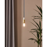 Dimmable LED G9 capsule bulb lit warm white in a brass pendant fitting, shown against a muted pink wall with curtain and plant in the background.
