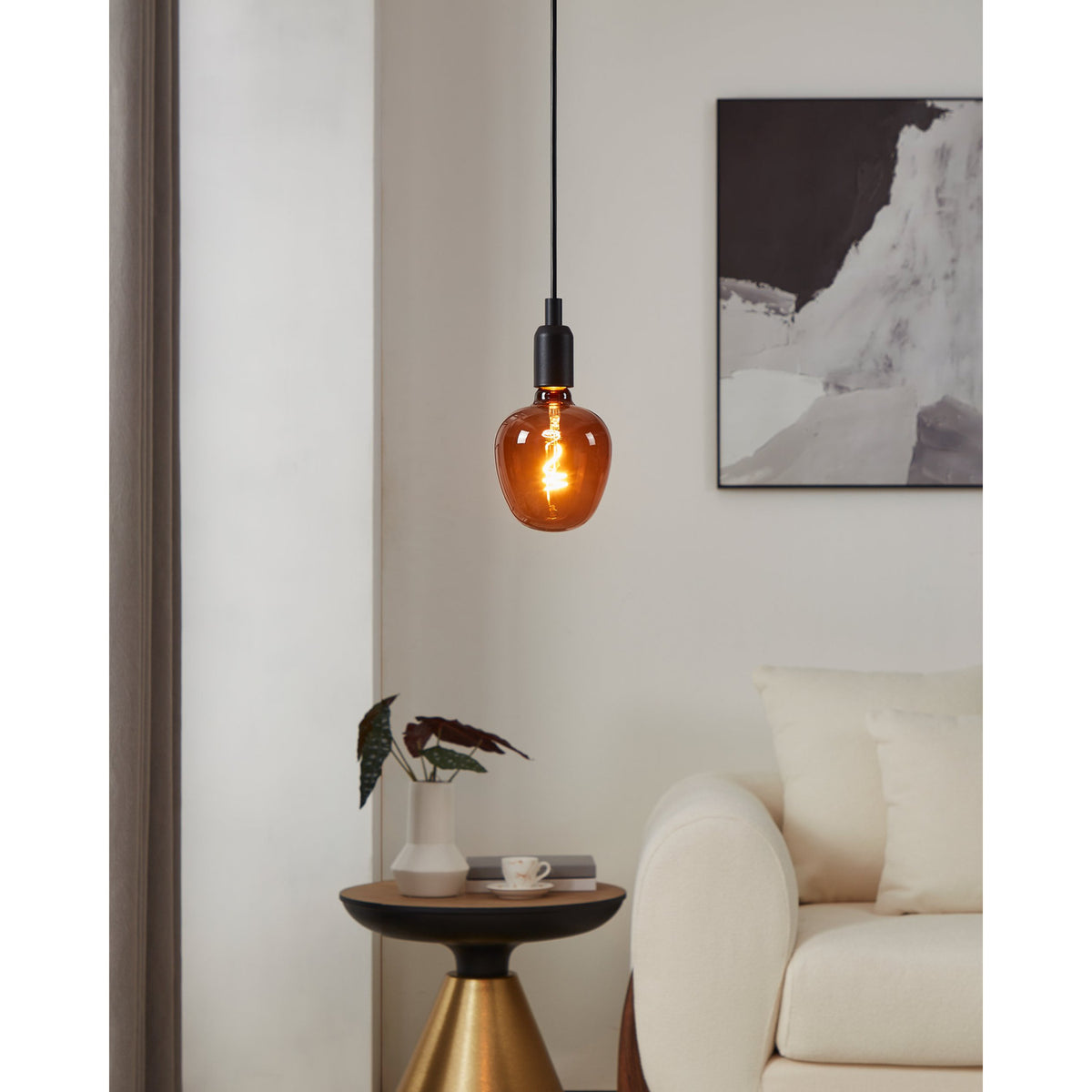 Dimmable LED globe bulb, E27 fitting, G125 amber-tinted glass with visible spiral filament, shown lit on a black pendant cord above a living room side table.
