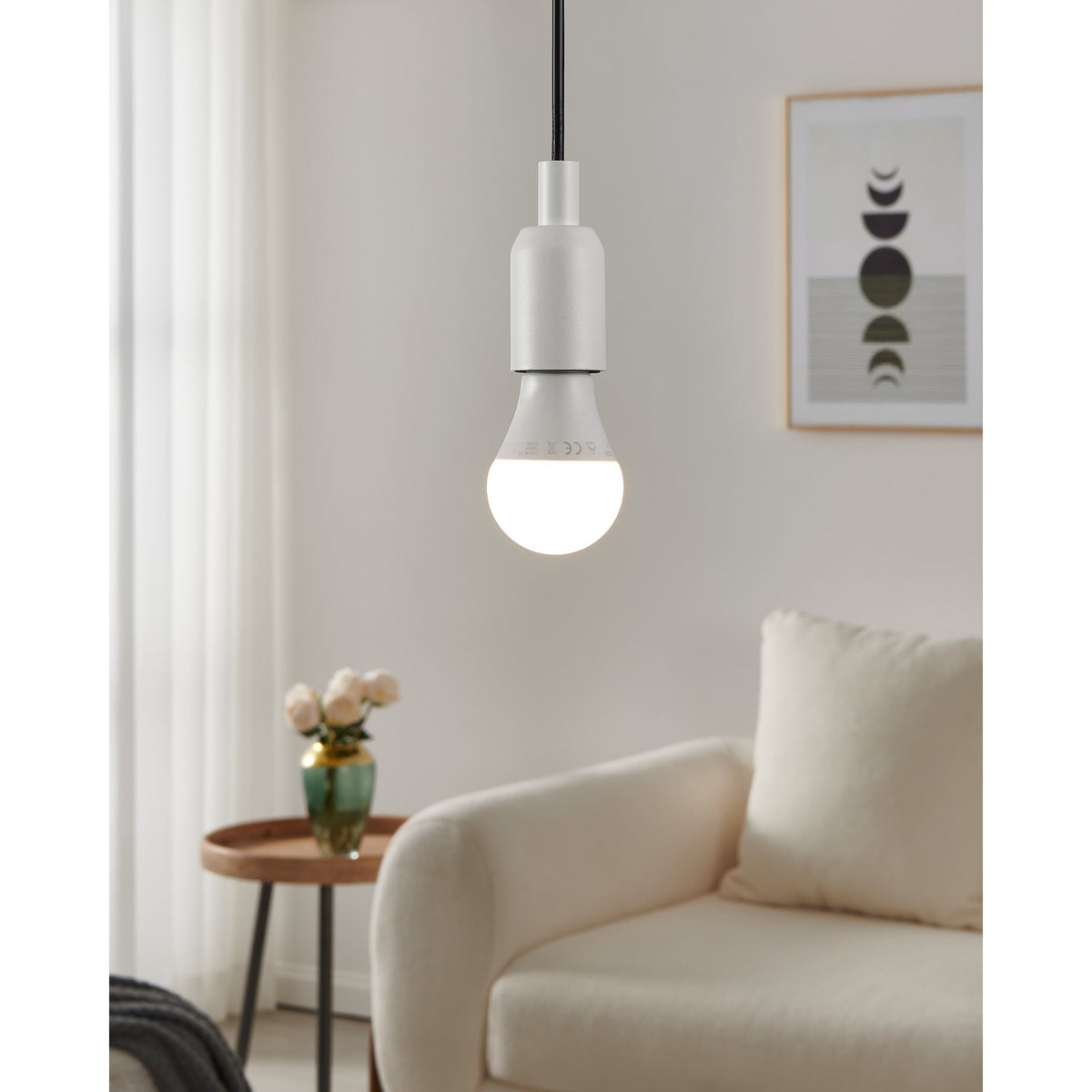 Dimmable LED GLS bulb, E27 screw cap, opal dome lit warm white, shown fitted in a pendant light fixture above a sofa in a living room.