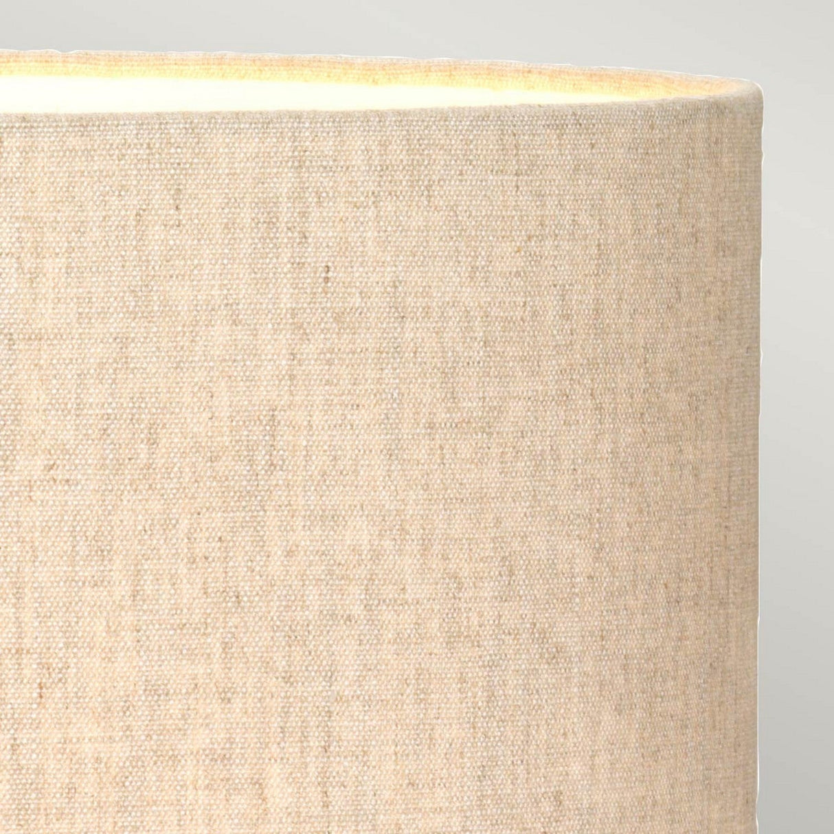 A detailed view of the Amelia-1 Table Lamp's beige fabric shade reveals its oval shape and smooth, woven texture. The upper section is softly illuminated, casting a warm glow against a light gray background that evokes the serene ambiance typical of a stag and fawn lamp.