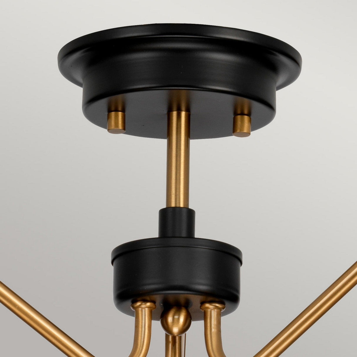 Here's a close-up of the Armand 3 Light Pendant Semi-Flush, showcasing a modern ceiling light fixture with an aged brass plated circular base. The design is enhanced by charcoal black paint accents and features multiple gold rods extending from the center, creating an elegant and contemporary appearance.